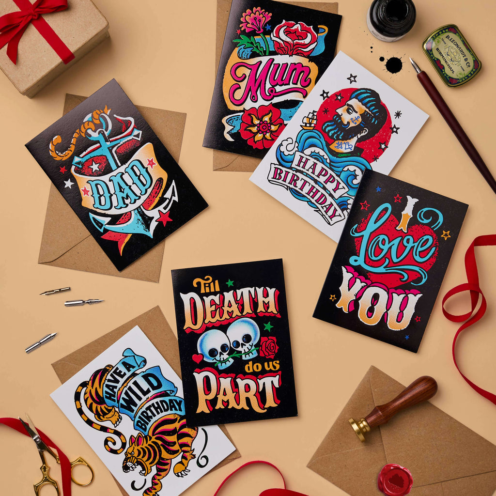 Flat lay of the ‘Inked’ collection cards: A mix of tattoo-inspired greeting cards, including “Til Death Do Us Part,” “Love You,” “Happy Birthday,” and more, paired with recycled craft envelopes. Designs feature vibrant colours, vintage typography, and striking foil finishes.