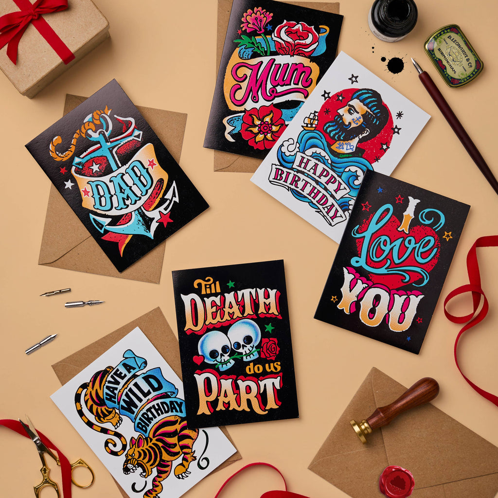 A mix of tattoo-inspired greeting cards, including “Til Death Do Us Part,” “Love You,” “Happy Birthday,” and more, paired with recycled craft envelopes. Designs feature vibrant colours, vintage typography, and striking foil finishes.