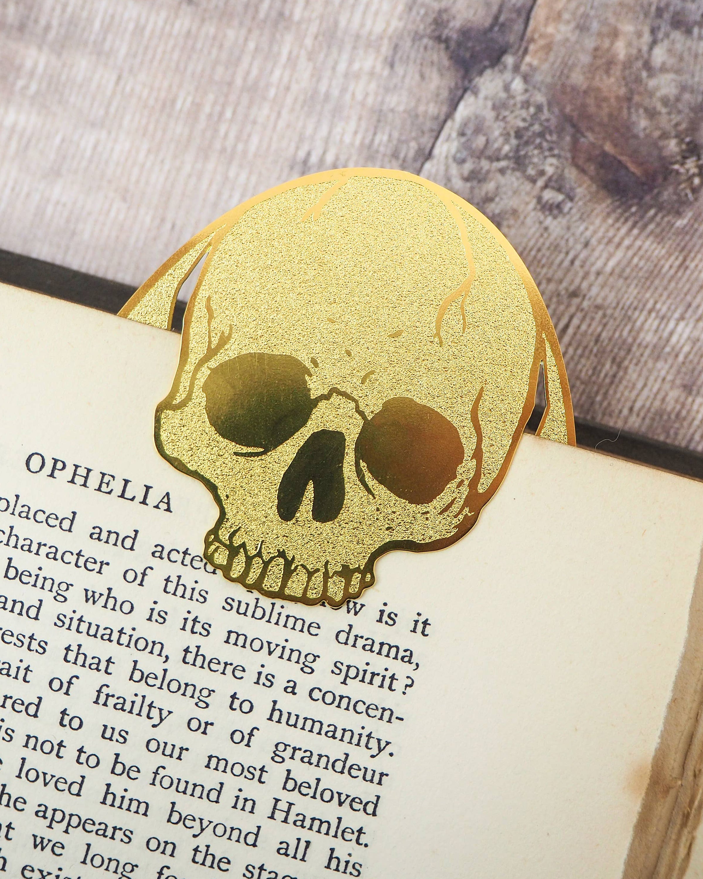 Gold brass skull bookmark by Literary Emporium clipped over a vintage Hamlet book page. Sold by Rebel Romance, a UK brand celebrating alternative style, gothic homeware and unique gifts for millennials.