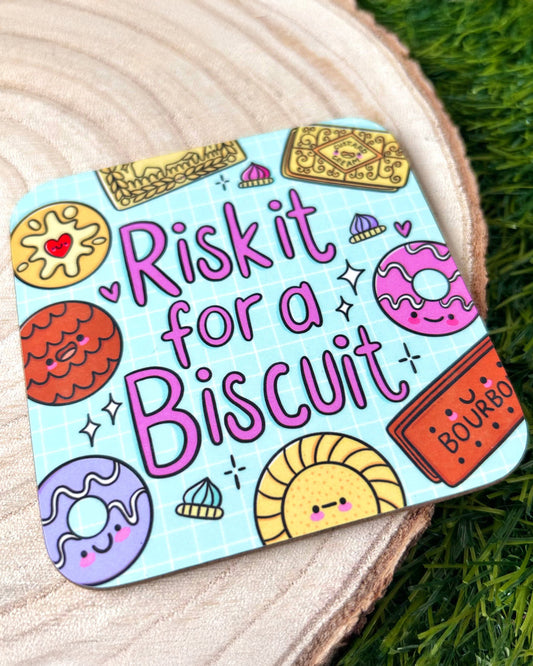 A square Rebel Romance coaster illustrated by Kelly Lou with the phrase “Risk It For A Biscuit” in pink text on a blue grid background, surrounded by cute cartoon biscuits including custard creams, bourbons and jam rings. Fun homeware gift from a UK small business celebrating alternative style.