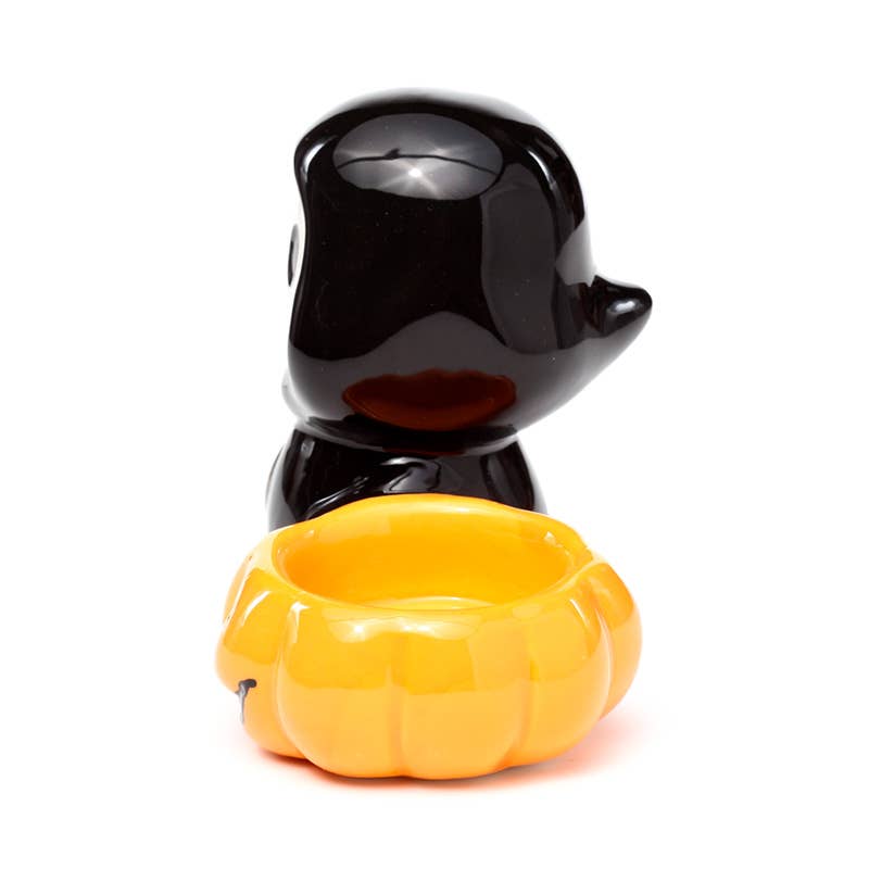Side angle of the Ceramic Skull Boy Tea Light Holder by Rebel Romance. The cute skull-faced figure in a black cloak stands beside a carved orange jack-o'-lantern bowl—ideal for Halloween table décor or gifting.