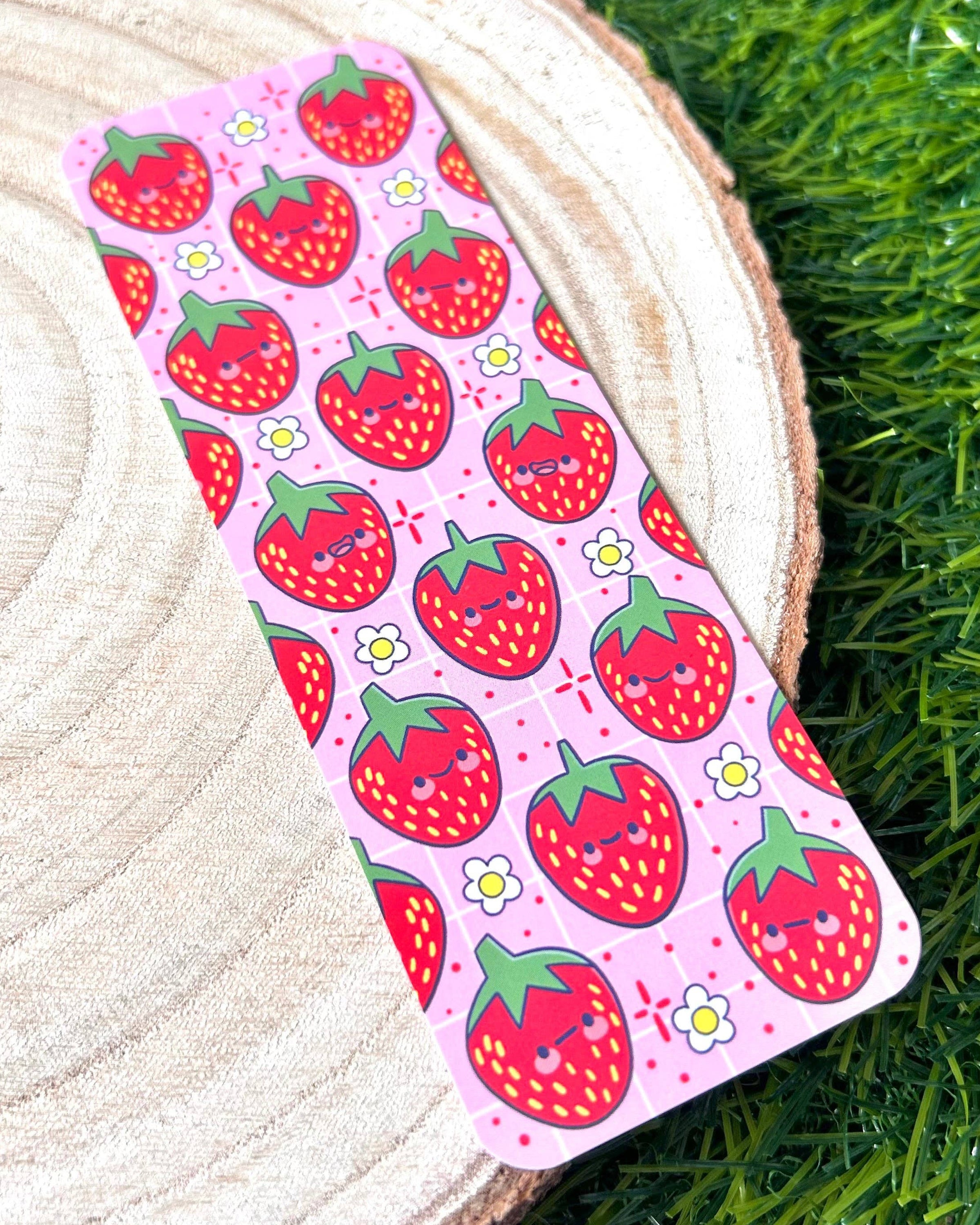 A vibrant Berry Cute Strawberries Bookmark by Kelly Lou from Rebel Romance. This pink bookmark features a repeating pattern of smiling red strawberries with green tops and tiny white flowers, illustrated by Kellylou. Perfect for millennial book lovers who adore quirky, alternative stationery.