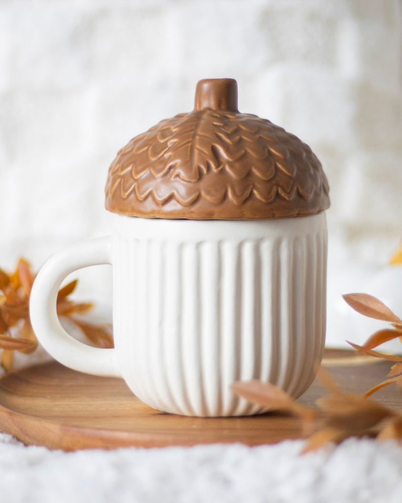 Lifestyle image of Rebel Romance’s Autumn Acorn Mug on a wooden tray with cosy leaves around it. The perfect mug for autumn tea or coffee in a nature-inspired home.