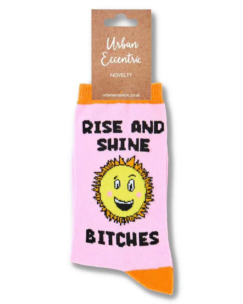 Urban Eccentric pink sock in packaging, labelled with kraft cardboard tag. Sock features a yellow sun character and slogan “Rise and Shine Bitches.” Available from Rebel Romance, a UK brand known for quirky, alternative style.