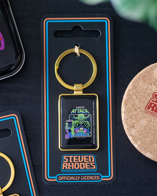 Anxiety Attack keyring by Steven Rhodes photographed on backing card with gold ring detail. Features retro horror arcade design with neon artwork. Stocked by Rebel Romance, a UK small business selling alternative gifts, gothic fashion and nostalgic accessories.