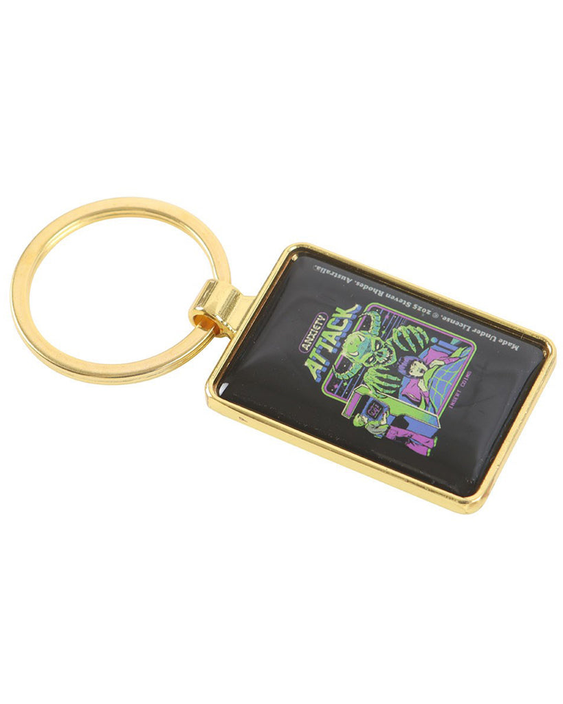 Gold metal Anxiety Attack keyring by Steven Rhodes, shown at an angle to highlight the rectangular enamel design. Features retro neon arcade-style artwork with a monster and child. Available at Rebel Romance, a UK indie brand for alternative style, gothic gifts and quirky accessories.