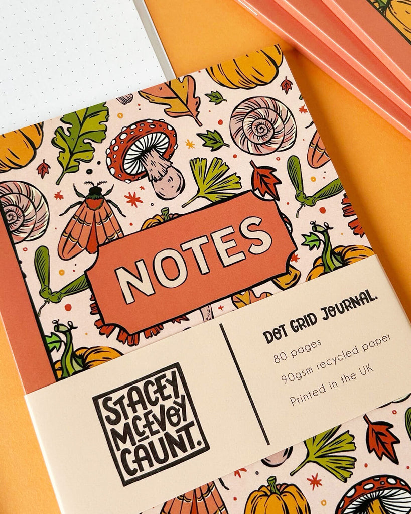 A close-up of the notebook front cover with the word “NOTES” framed in orange. The cream band displays details: “Dot Grid Journal, 80 pages, 90gsm recycled paper, Printed in the UK.”