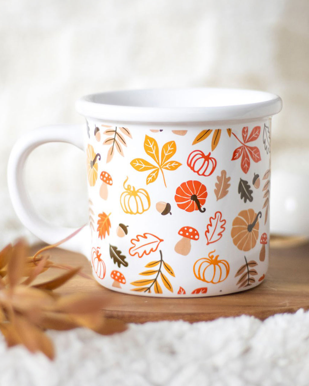 The mug placed on a soft, fluffy surface with autumn leaves scattered around. The warm tones of the mug’s print complement the cosy autumn aesthetic.