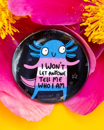 Rebel Romance round badge displayed on vivid pink and yellow flower petals. The design features an axolotl in trans flag colours with the words “I won’t let anyone tell me who I am”. A bold celebration of identity, illustrated by Katie Abey.