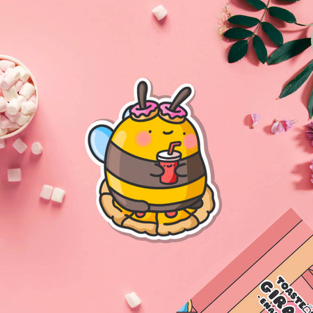 Cute cartoon-style vinyl sticker of a bumblebee with pink doughnut antennae, holding a red drink and sitting on a pie. Ideal for laptops, bottles, and journals.