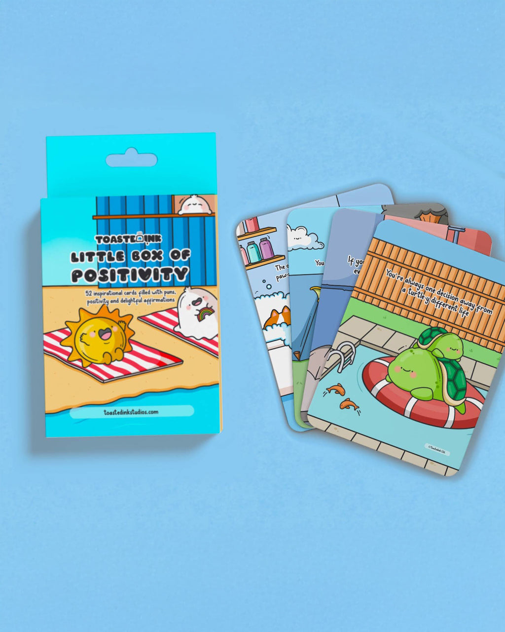 A blue box titled “Little Box of Positivity” surrounded by several colourful Toastedink affirmation cards with punny, illustrated designs.