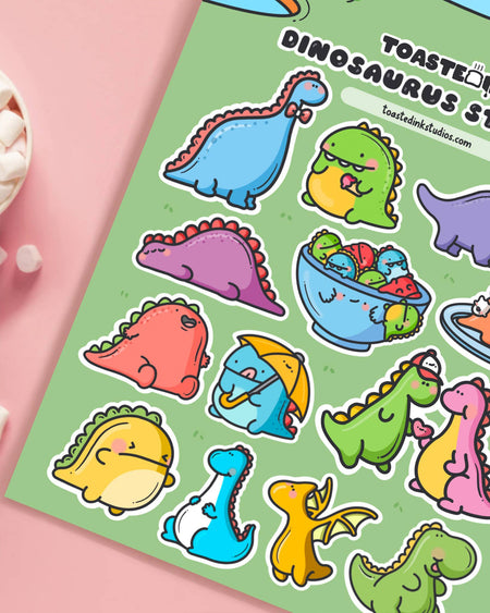 Close-up of Toastedink's Dinosaurus Sticker Sheet on a pink background. Features kawaii-style dinosaurs in a variety of colours and poses, perfect for decorating planners, letters, and more. Stocked by Rebel Romance.