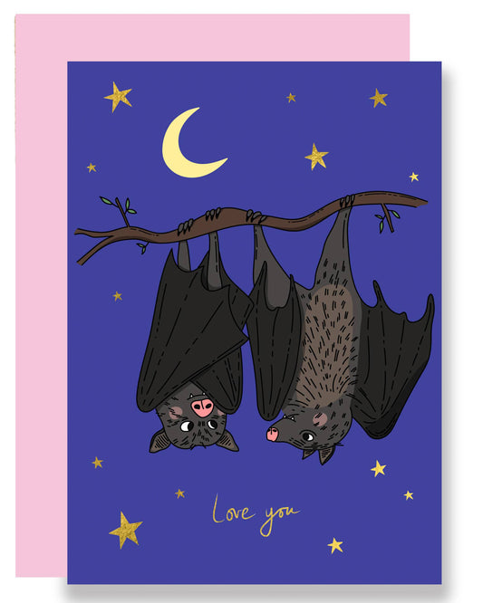 Illustrated love card featuring two cute bats hanging upside down from a branch under a crescent moon and golden stars, with the words “Love you” in gold foil, paired with a pink envelope.