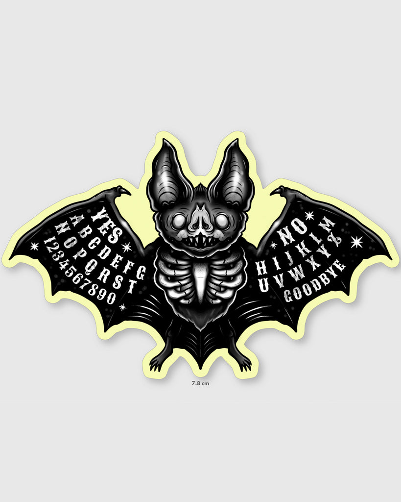 Glow in the dark Ouija bat sticker featuring spooky black and white bat with skeleton body and spirit board-inspired wings. Artwork by MilkTeef with YES, NO, letters, and numbers printed on each wing. Perfect gothic vinyl sticker for laptops, notebooks, and altars. Designed for Halloween and alternative style lovers.