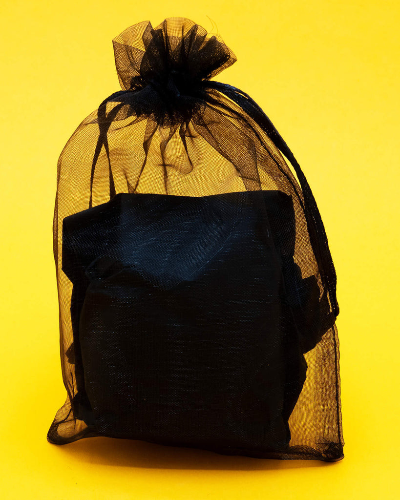 A handmade Katie Abey x Ghost Of The Month needle felted ghost cat shown packaged inside a sheer black gift bag on a bold yellow background. The felted wool ghost cat is approx 8cm by 5cm and makes a unique decorative gift for quirky art lovers and collectors of handmade creatures.