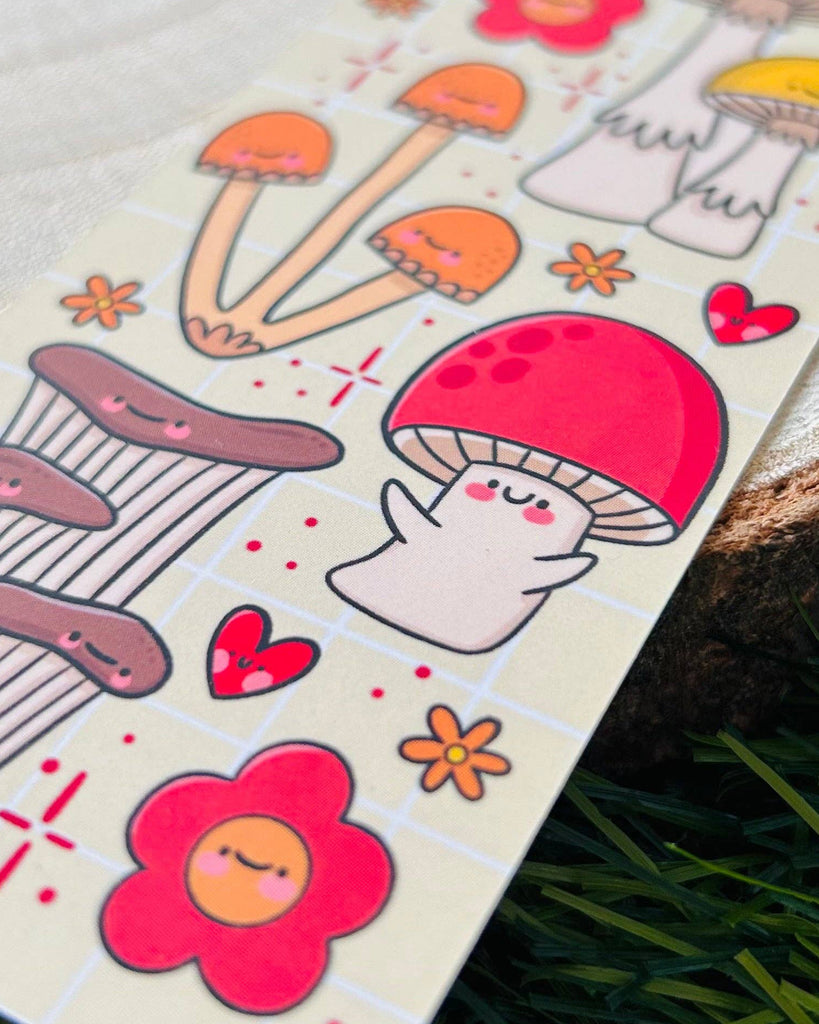Close-up of the Fungi Cuties Bookmark by Kelly Lou, a velvet-laminated bookmark with smiling mushrooms and flowers. A whimsical, pastel-toned design available at Rebel Romance, a UK small biz that loves all things magical and alternative.