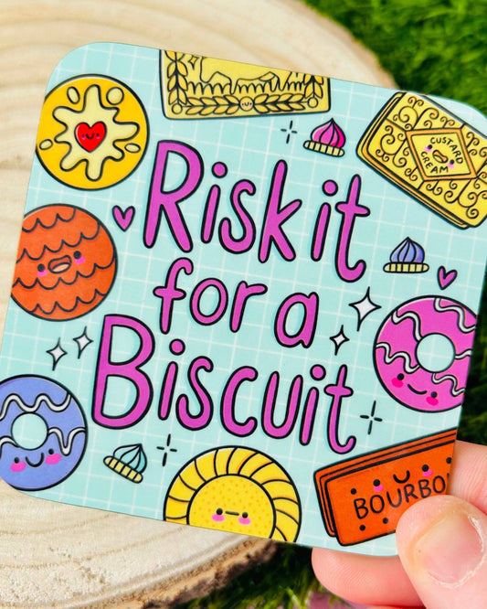 Close-up of a Rebel Romance “Risk It For A Biscuit” coaster designed by Kelly Lou, featuring colourful illustrated biscuits such as bourbons, custard creams and jam rings on a blue grid background. A quirky homeware piece from a UK brand known for alternative fashion and gifts.