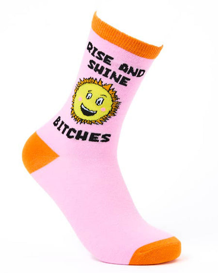 Pink novelty sock with orange toe, heel, and cuff, featuring a smiling sunshine graphic and bold black text that reads "Rise and Shine Bitches." Designed by Urban Eccentric and stocked by Rebel Romance, a UK small business celebrating alternative fashion and quirky style.