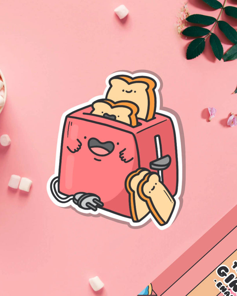 Cute toaster vinyl sticker on a pink background, featuring a red smiling toaster with two happy slices of toast popping up. Surrounded by mini marshmallows and flowers. Designed by Toastedink and stocked by Rebel Romance, a UK small business embracing quirky, alternative style.
