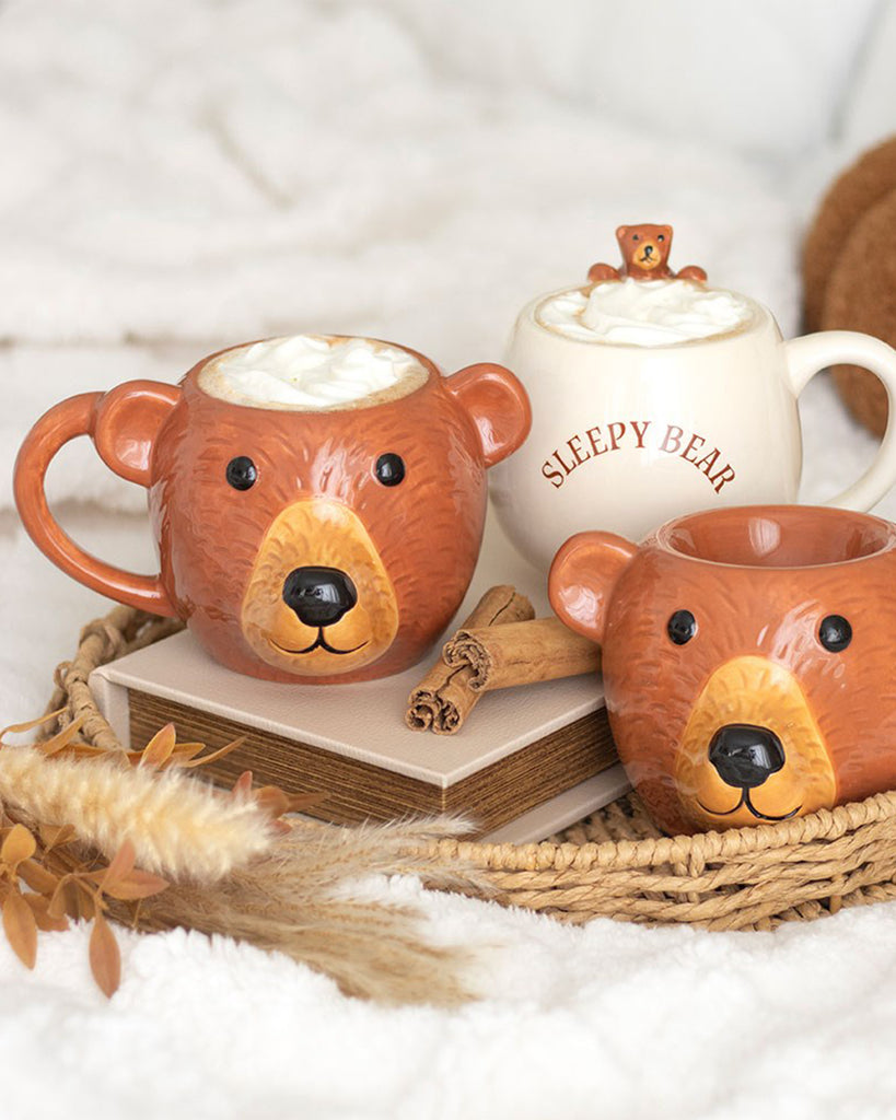 Lifestyle shot featuring the Rebel Romance Bear Shaped Mug, a bear shaped wax warmer and a white “Sleepy Bear” mug filled with cream, displayed on books and a woven tray. Perfect for cosy mornings and adorable gift ideas.