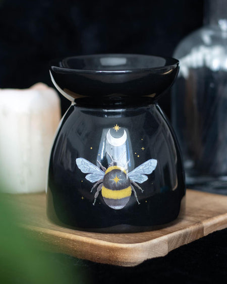 the Forest Bee Oil Burner on a wooden tray, surrounded by candles and glass jars, creating a cosy, witchy aesthetic.