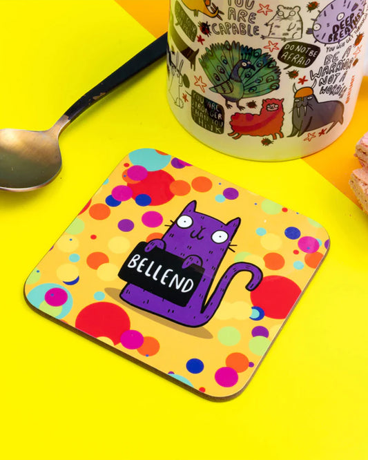 Funny coaster with a cartoon purple cat holding a sign that says “Bellend” against a colourful polka dot background. Designed by Katie Abey. 9cm square with rounded corners. Made in the UK. A perfect gift for cat lovers with a cheeky sense of humour.