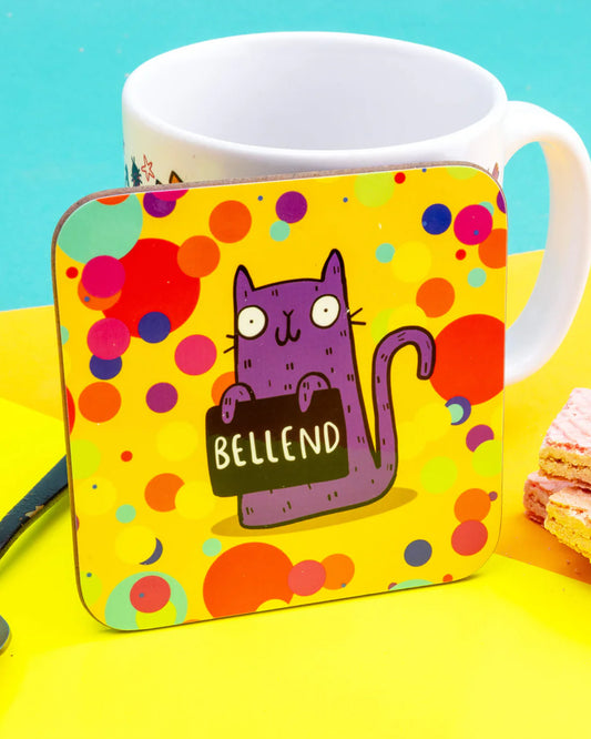 a coaster of a purple cat on a yellow confetti spotty background smiling holding a sign saying 'BELLEND' designed by Katie Abey in the UK