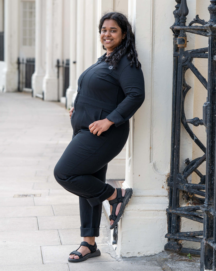 Model Vidhya stands relaxed in front of ornate black railings wearing the Rebel Romance Jet Black Boiler Suit. With rolled cuffs and flattering seams, this look is both timeless and edgy.