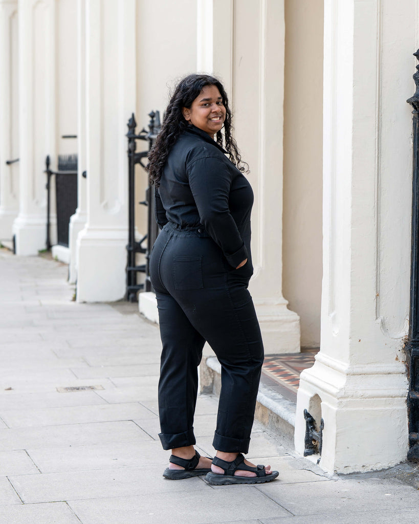 Back view of Vidhya walking confidently in the Rebel Romance Jet Black Boiler Suit, showcasing the flattering cut, cuffed hems, and utility-inspired details. A slow fashion staple with serious attitude.