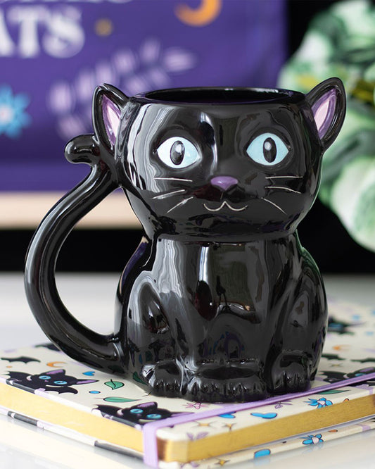 Rebel Romance Cute and Creepy Black Cat Mug sitting on a matching cat-themed notebook with a purple strap. Featuring a high-gloss ceramic finish and vivid facial features, this mug is perfect for those who love magical, witchy homeware and cute gothic cats.