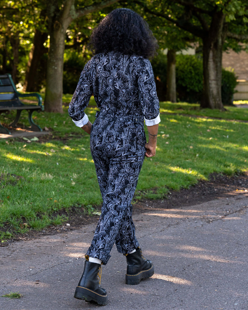 Jasmine wears the Rebel Romance Black Floral Cobweb Boilersuit, showing the back design. The all-over floral and cobweb print covers the black stretch twill fabric. Ethical and inclusive slow fashion brand.