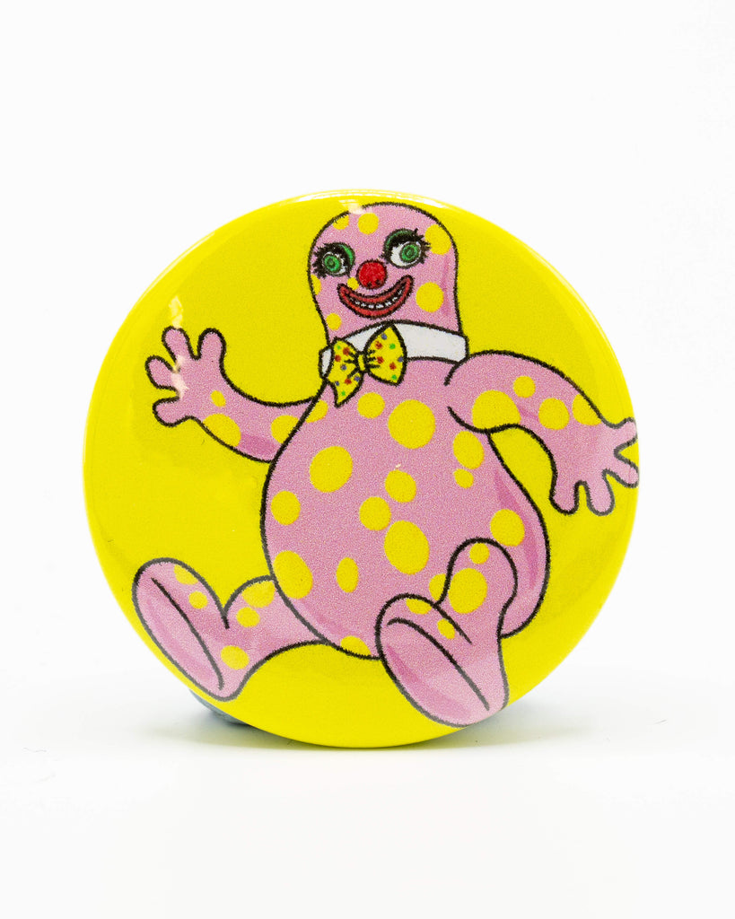 Round button pin badge from Rebel Romance featuring a bright yellow background and a playful pink character with yellow spots, red clown nose, green eyes, and a yellow polka dot bow tie. Designed by Bite Your Granny. A bold, nostalgic accessory perfect for lovers of alternative fashion and kitsch style.