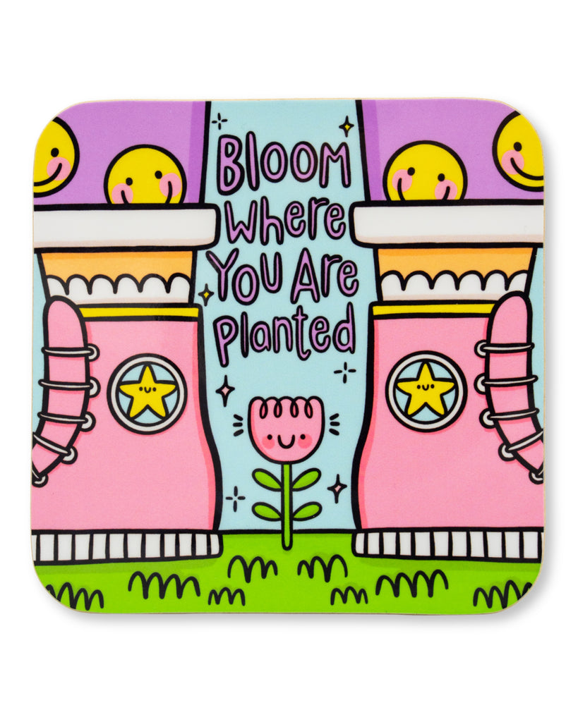 Colourful drinks coaster by Kelly Lou featuring pink boots with smiley stars and the uplifting quote Bloom Where You Are Planted surrounded by bright green grass and pastel purple sky with a glossy finish made from durable hardboard MDF
