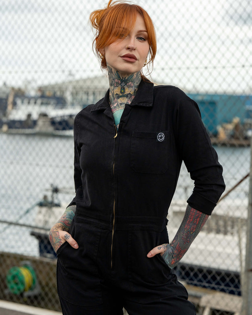 Close-up of Erin in the black boiler suit, showing the chest pocket with a small Rebel Romance logo patch.