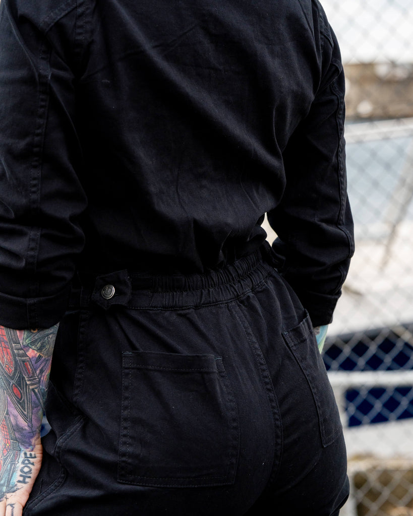 Erin turns slightly to show the back of the boiler suit, highlighting the stretchy back panel and pocket details.