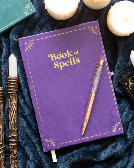Styled flat lay of the Book of Spells journal and amethyst pen, surrounded by candles, crystal wands, and other witchy accessories, perfectly fitting Rebel Romance's alternative aesthetic.