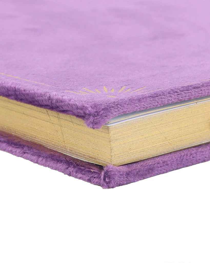 Close-up of the Book of Spells journal corner, highlighting the luxurious purple velvet cover with gold foiled detailing. The pages have shimmering gold edges, adding a magical touch to the journal.