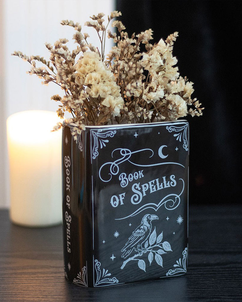The Rebel Romance Book of Spells vase styled on a black surface with dried flowers and a glowing candle. Perfect for gothic or witchy interior vibes with a dark academia twist.