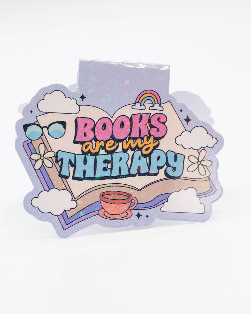 Glittery pastel magnetic bookmark from Rebel Romance with a dreamy design featuring an open book, clouds, a rainbow, flowers, sunglasses, and a tea cup. Bold text reads “Books Are My Therapy” in multicoloured lettering. A perfect gift for bookworms and daydreamers who find comfort in reading. Great for millennials who love cute, alternative stationery with a whimsical twist.