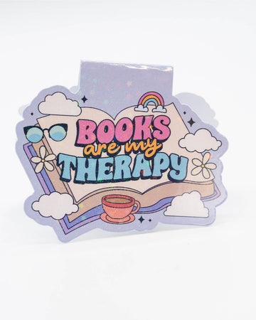 Glittery pastel magnetic bookmark from Rebel Romance with a dreamy design featuring an open book, clouds, a rainbow, flowers, sunglasses, and a tea cup. Bold text reads “Books Are My Therapy” in multicoloured lettering. A perfect gift for bookworms and daydreamers who find comfort in reading. Great for millennials who love cute, alternative stationery with a whimsical twist.