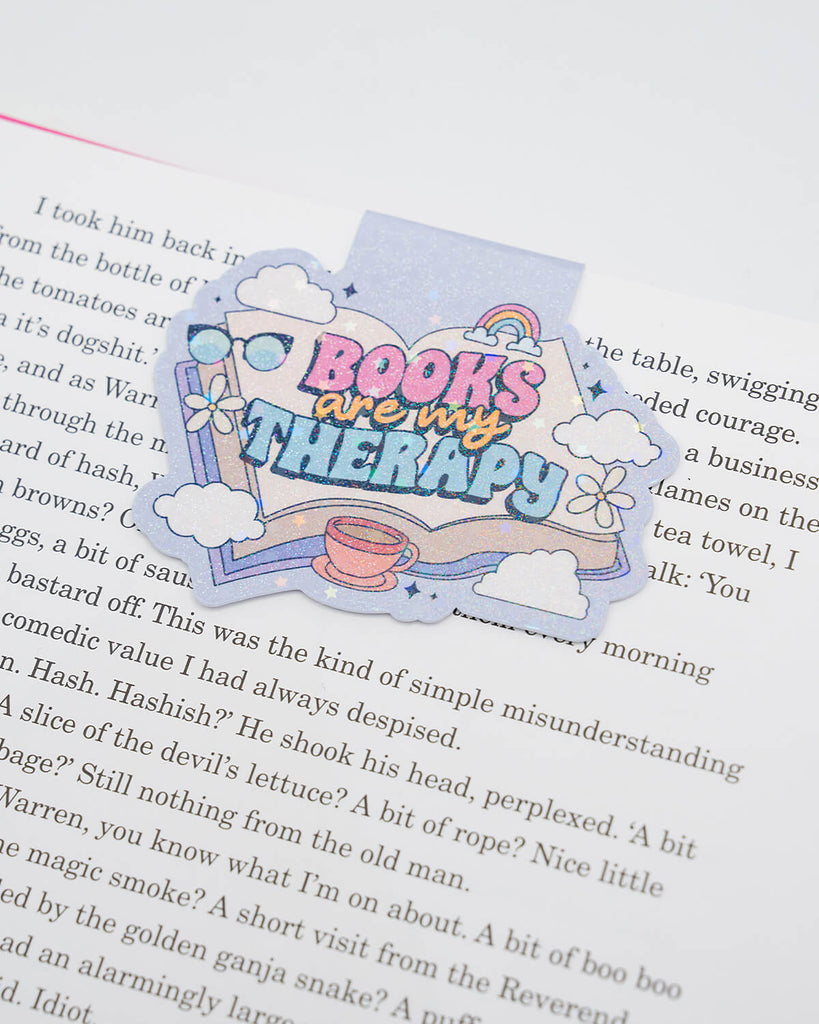 Whimsical magnetic bookmark clipped onto a book page, shaped like a sparkly pastel cloud scene with the phrase “Books Are My Therapy.” Features illustrations of a book, rainbow, coffee cup, and daisy flowers. Ideal for book lovers who use reading for relaxation. A fun, functional gift from Rebel Romance for millennials who enjoy cosy, aesthetic reading accessories.