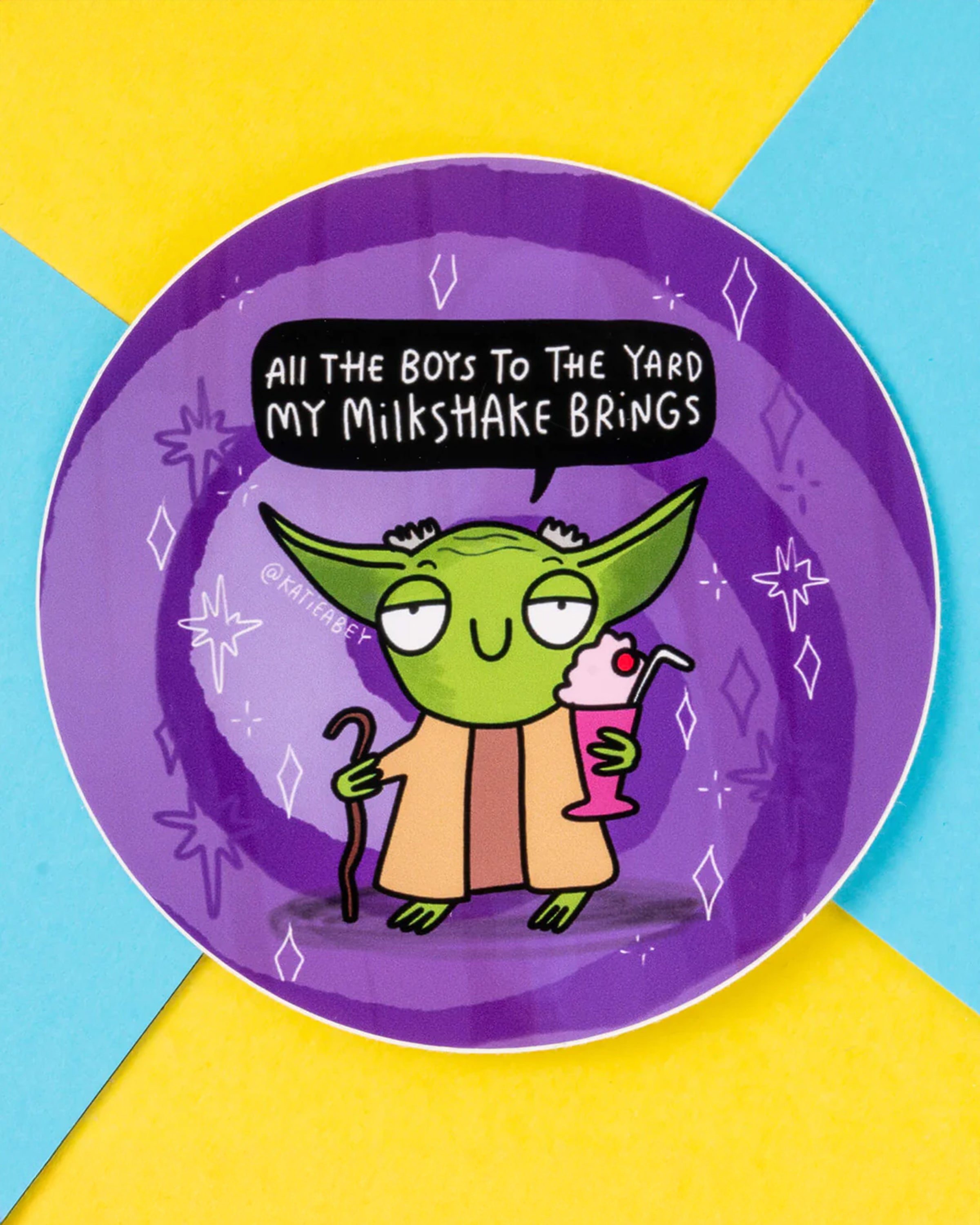 Circular sticker showcasing a green alien-inspired character holding a pink milkshake and a cane, with a speech bubble that reads, 