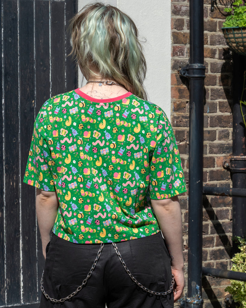Back view of Faeryn in the Rebel Romance x Dipstick Store Bugs Cropped Boxy Tee. The green top is covered in a dopamine-bright bug and flower print. Styled with black cargo trousers and chains. Ethical fashion for dopamine dressers from UK brand Rebel Romance.