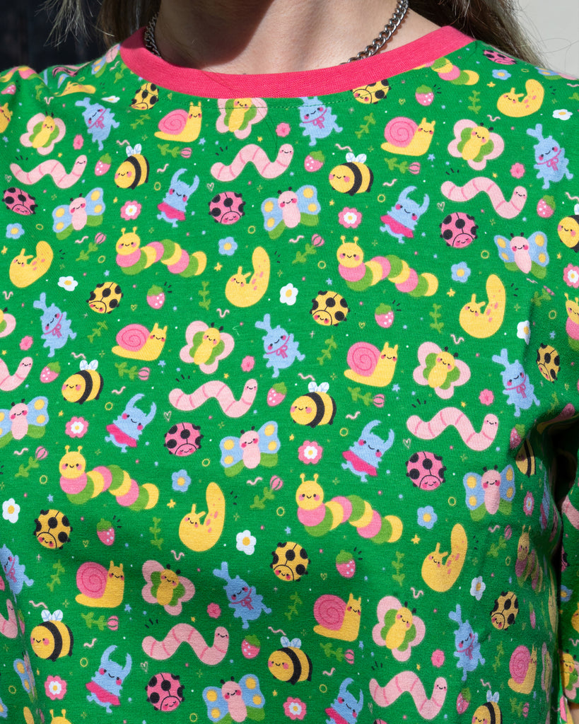 Close-up of the Rebel Romance x Dipstick Store Bugs Cropped Boxy Tee contrasting hot pink neck, showing the pastel bug print featuring worms, snails, bees, butterflies, and flowers on a bright green background. Inclusive and ethical slow fashion from UK business Rebel Romance.
