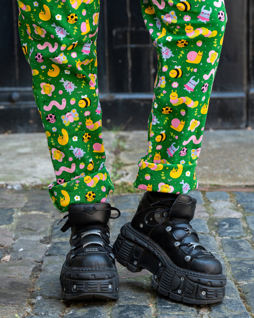 Close-up of the lower legs and chunky black platform boots styling Rebel Romance x Dipstick Store Bugs Stretch Dungarees. The green fabric shows bright bug and flower illustrations, celebrating fun, bold, and ethical UK alternative fashion.