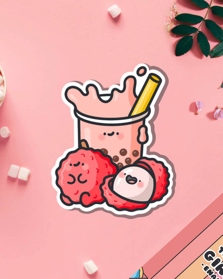 Cute vinyl sticker of a smiling lychee bubble tea cup with two cheerful lychee fruits, on a pink background with marshmallows and petals. Designed by Toastedink and stocked by Rebel Romance, a UK brand celebrating alternative and kawaii style. Perfect for decorating laptops, water bottles, and notebooks.