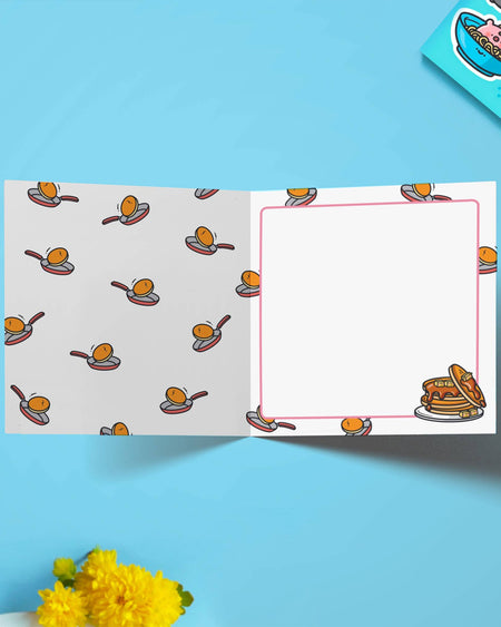 Open view of the pancake cat birthday card, revealing a blank message space bordered with tiny illustrations of a pancake in a frying pan. Designed by Toastedink and sold by Rebel Romance, a UK alternative lifestyle brand celebrating whimsy and weirdness.
