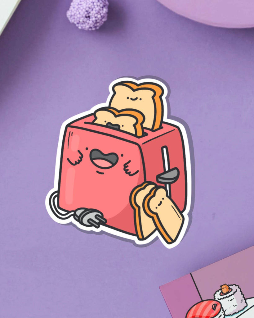 Toaster vinyl sticker on a pastel purple surface with a red cartoon toaster and two smiling slices of toast. Stocked by Rebel Romance, a UK brand celebrating whimsical and alternative aesthetics for millennials.