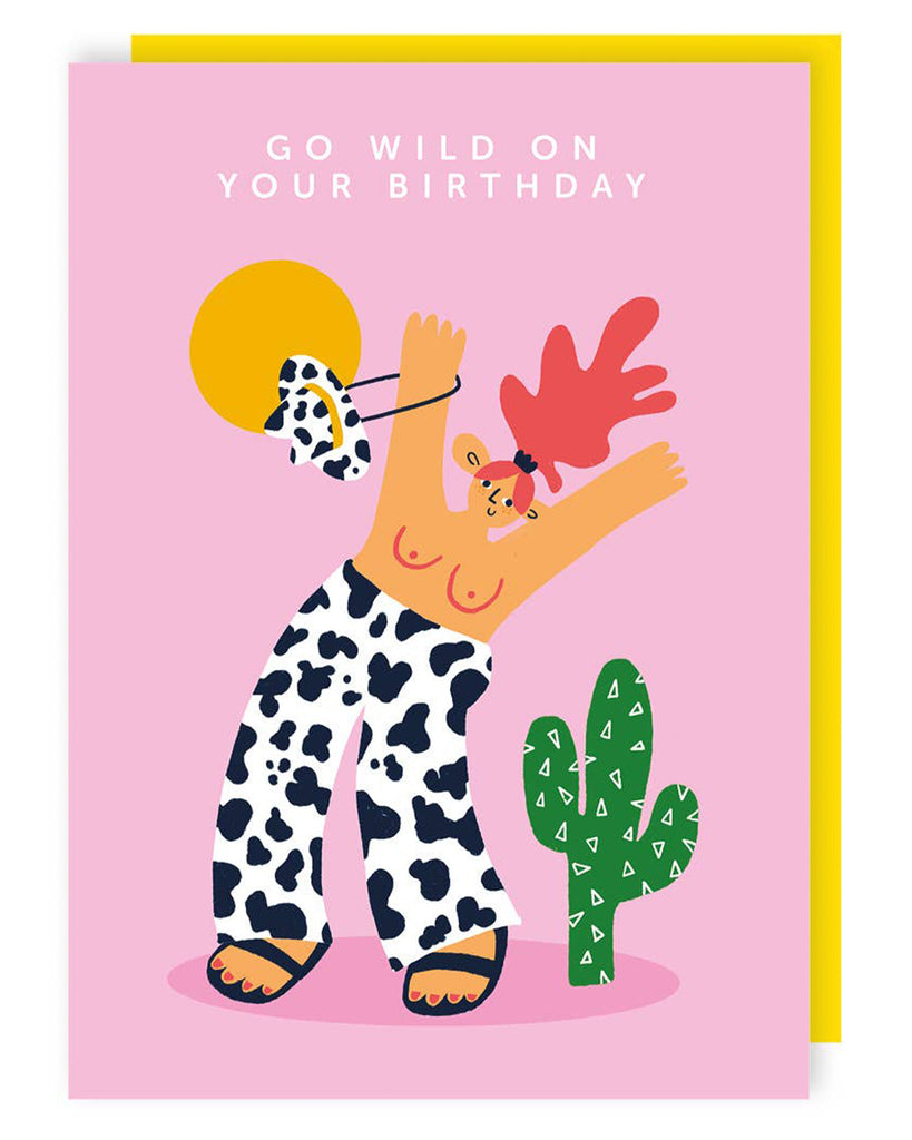 A colorful birthday card featuring a cartoon character with red hair and a cow-print outfit, swinging a spotted cowboy hat, with a green cactus and a bright yellow sun in the background. The text on the card reads 'GO WILD ON YOUR BIRTHDAY'.