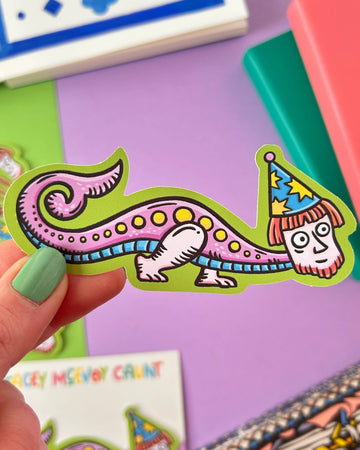 Colourful waterproof vinyl sticker from Rebel Romance featuring a quirky, long-bodied wizard creature inspired by medieval marginalia, wearing a starry hat with a human face. Set on a branded Stacey McEvoy Caunt backing card with a lilac background. Perfect for laptops, bottles, or gifting.